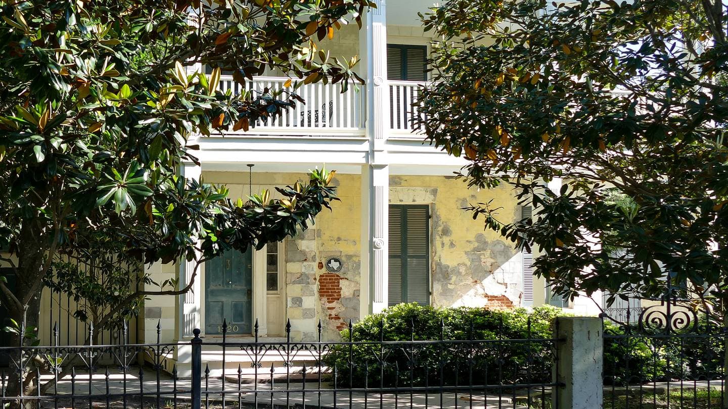 Historic two-story family home in Galveston, Texas behind an iron fence and magnolia trees
