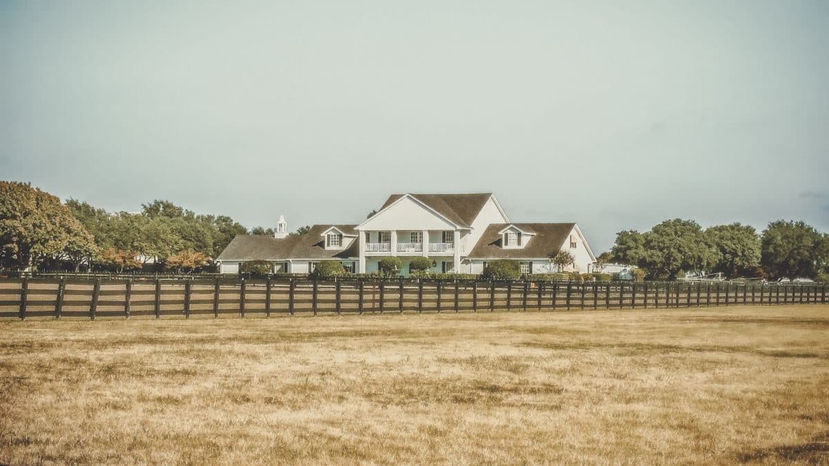 White ranch house behind a wooden fence on dry Texas grassland