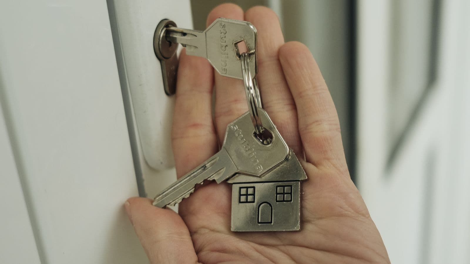 Hand holding house keys with a house-shaped keychain at a front door lock